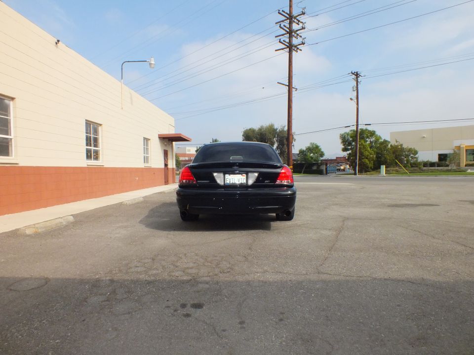 Black Crown Victoria sedan rear in parking lot beside building and power poles