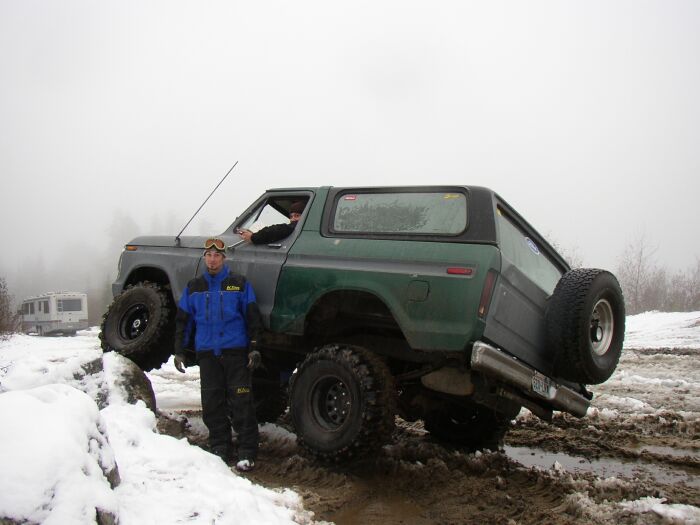 Lifted green and gray Ford Bronco flexed on a muddy snowy trail with man standing alongside