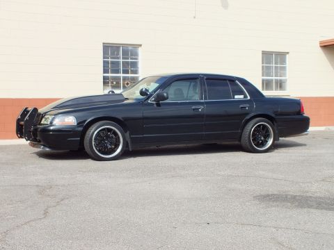 2003 Ford Crown Victoria - Lowered black Crown Victoria with push bar shown side-on against a tan masonry wall.