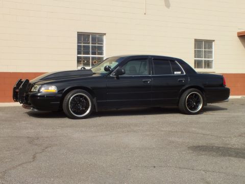 2003 Ford Crown Victoria - Side profile of a blacked-out Crown Victoria parked on cracked asphalt by a brick building.