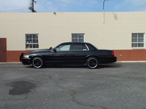 2003 Ford Crown Victoria - Profile view of a blacked-out Crown Victoria with front push bar against block wall.