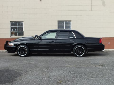 2003 Ford Crown Victoria - Glossy black Crown Victoria side profile with window visors and dark wheels by a brick wall.