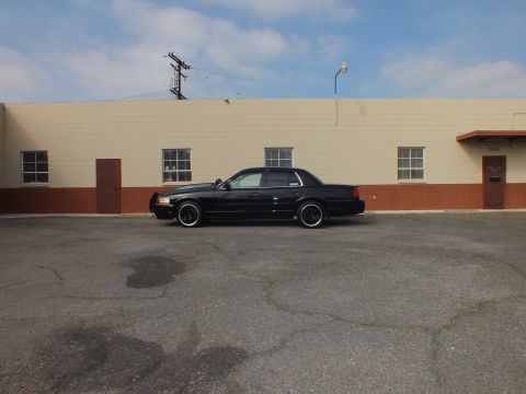 2003 Ford Crown Victoria - Distant side view of a black Crown Victoria in a lot beside a tan industrial building.
