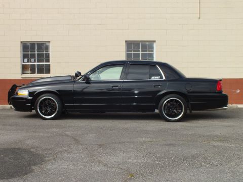 2003 Ford Crown Victoria - Blacked-out Crown Victoria shown side-on with window visors and front push bar.