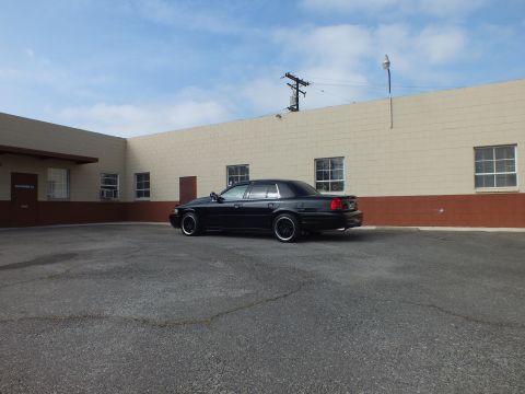 2003 Ford Crown Victoria - Black Crown Victoria parked in a wide lot, rear passenger angle against a tan building.