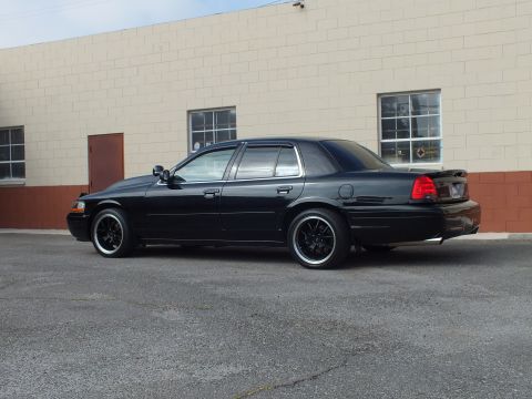2003 Ford Crown Victoria - Rear quarter of a blacked-out Crown Victoria with lip spoiler near a block warehouse.