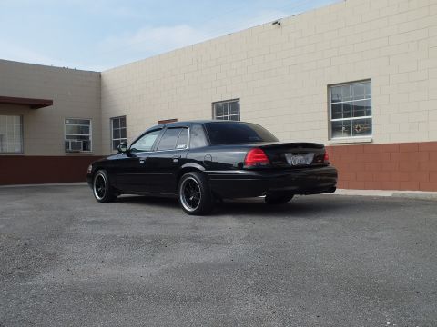 2003 Ford Crown Victoria - Blacked-out Crown Victoria rear quarter with lip spoiler against a block masonry wall.