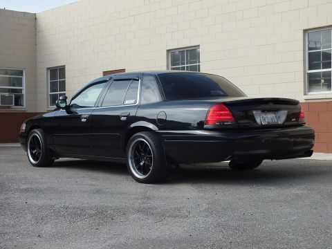 2003 Ford Crown Victoria - Rear quarter of a murdered-out Crown Victoria with window visors and lip spoiler.