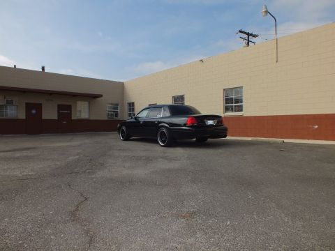 2003 Ford Crown Victoria - Distant rear view of a black Crown Victoria parked on cracked asphalt by a building.