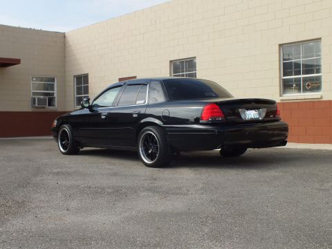 2003 Ford Crown Victoria - Blacked-out Crown Victoria rear quarter with lip spoiler against a tan block wall.