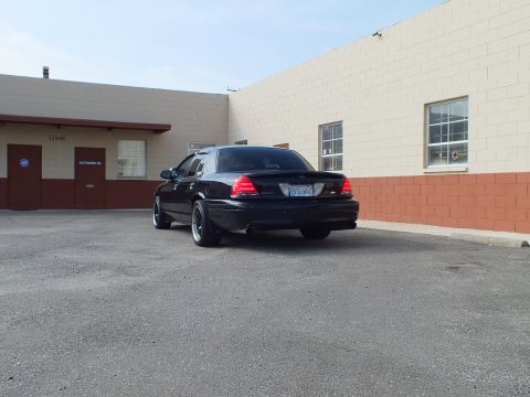 2003 Ford Crown Victoria - Rear view of a blacked-out Crown Victoria with dual exhaust by a tan block building.