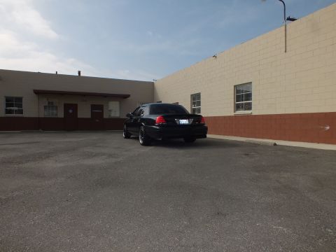 2003 Ford Crown Victoria - Distant rear view of a black Crown Victoria parked by a tan warehouse wall.