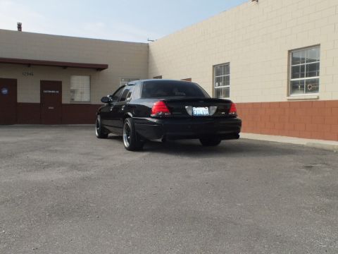 2003 Ford Crown Victoria - Rear quarter of a blacked-out Crown Victoria with SVT badge near a masonry wall.