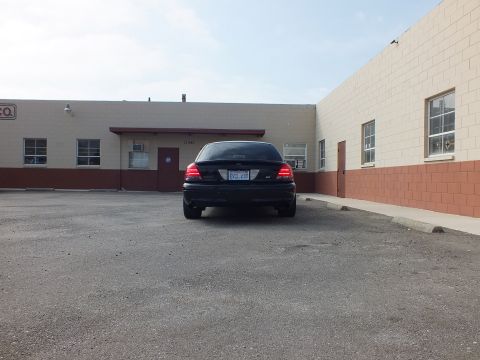 2003 Ford Crown Victoria - Rear of a black Ford Crown Victoria sitting in a paved lot in front of a tan masonry building.