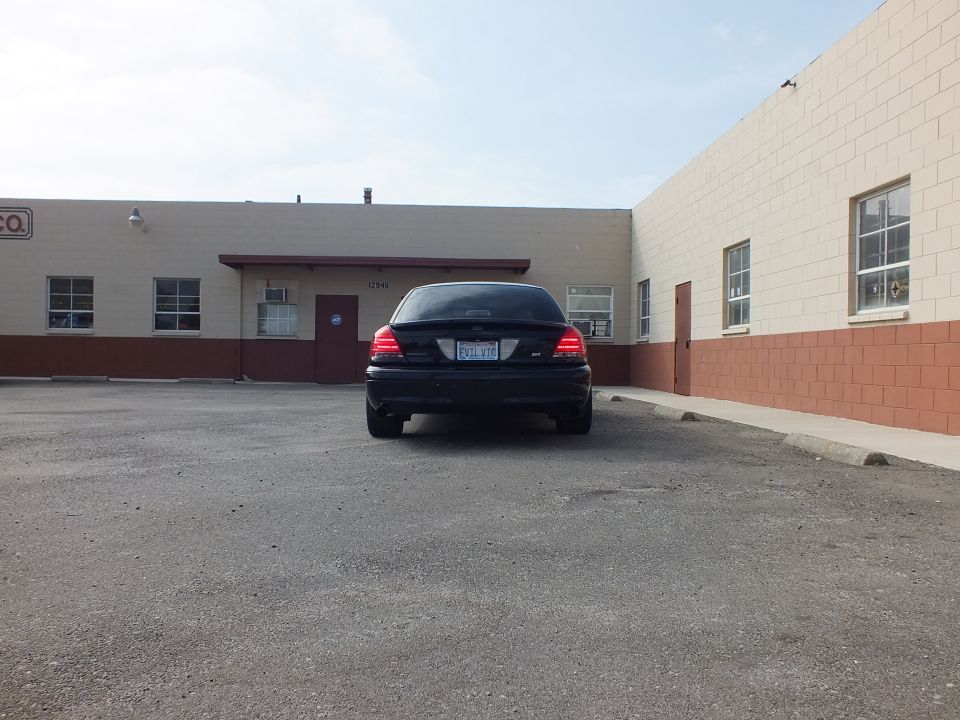Black Ford Crown Victoria sedan parked rear view facing tan industrial building