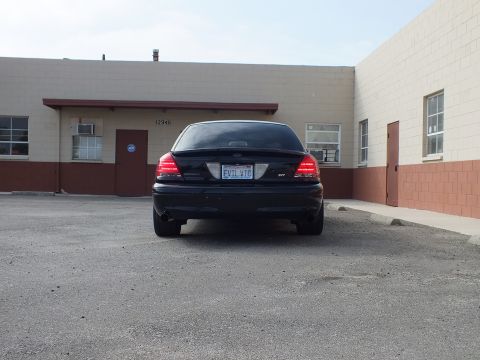 2003 Ford Crown Victoria - Black Crown Victoria sedan shown from behind, EVIL VIC plate, against a building numbered 12946.