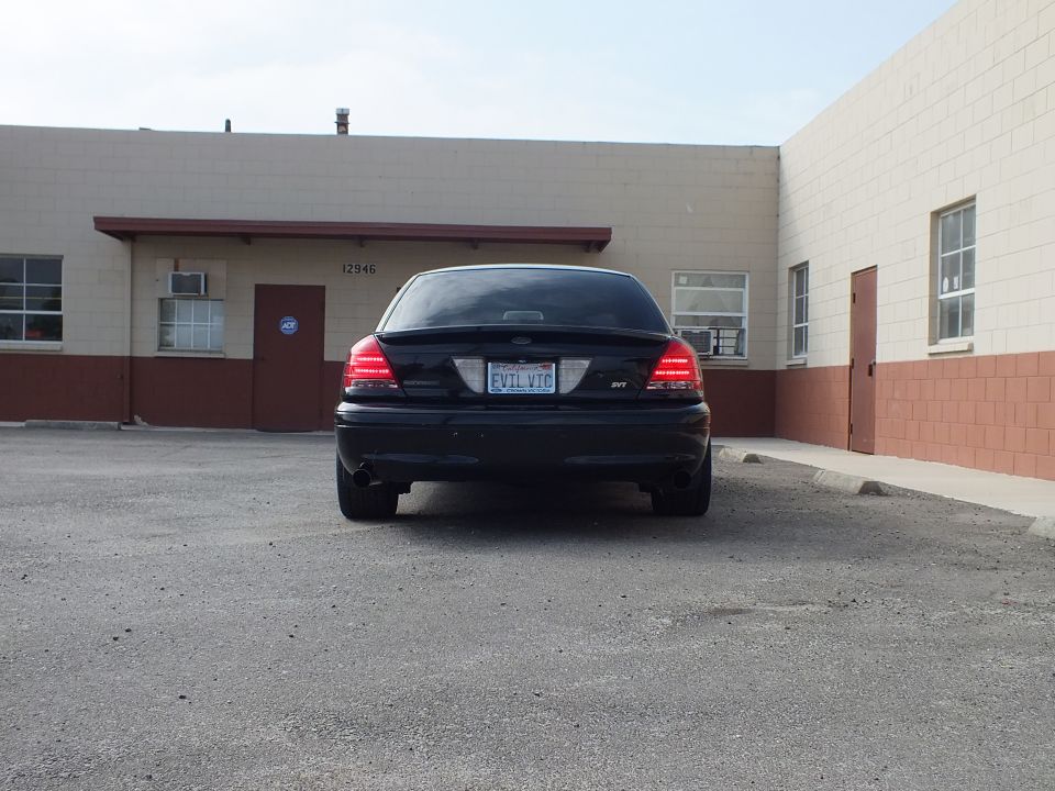 Black Ford Crown Victoria rear with EVIL VIC plate parked at building marked 12946