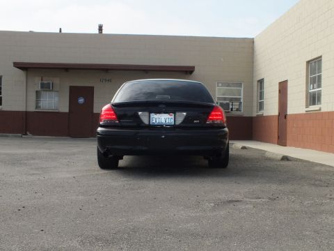 2003 Ford Crown Victoria - Black Crown Victoria SVT seen from behind in a lot, building numbered 12946 in background.