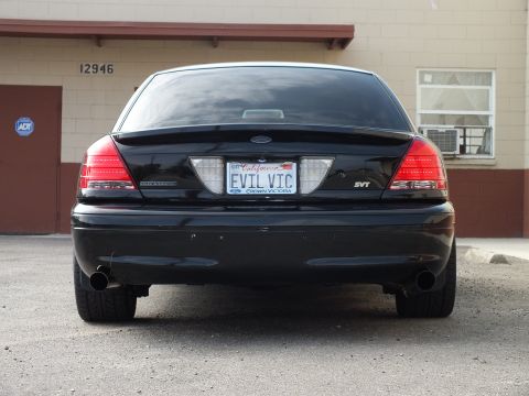 2003 Ford Crown Victoria - Rear of a lowered black Crown Victoria SVT with dual exhaust and EVIL VIC plate on cracked pavement.