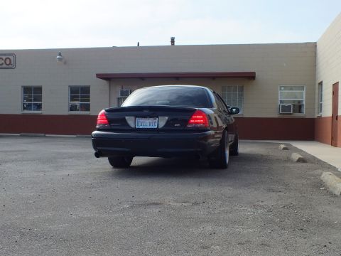 2003 Ford Crown Victoria - Rear three-quarter of a black Crown Victoria SVT parked near a tan building with an awning.