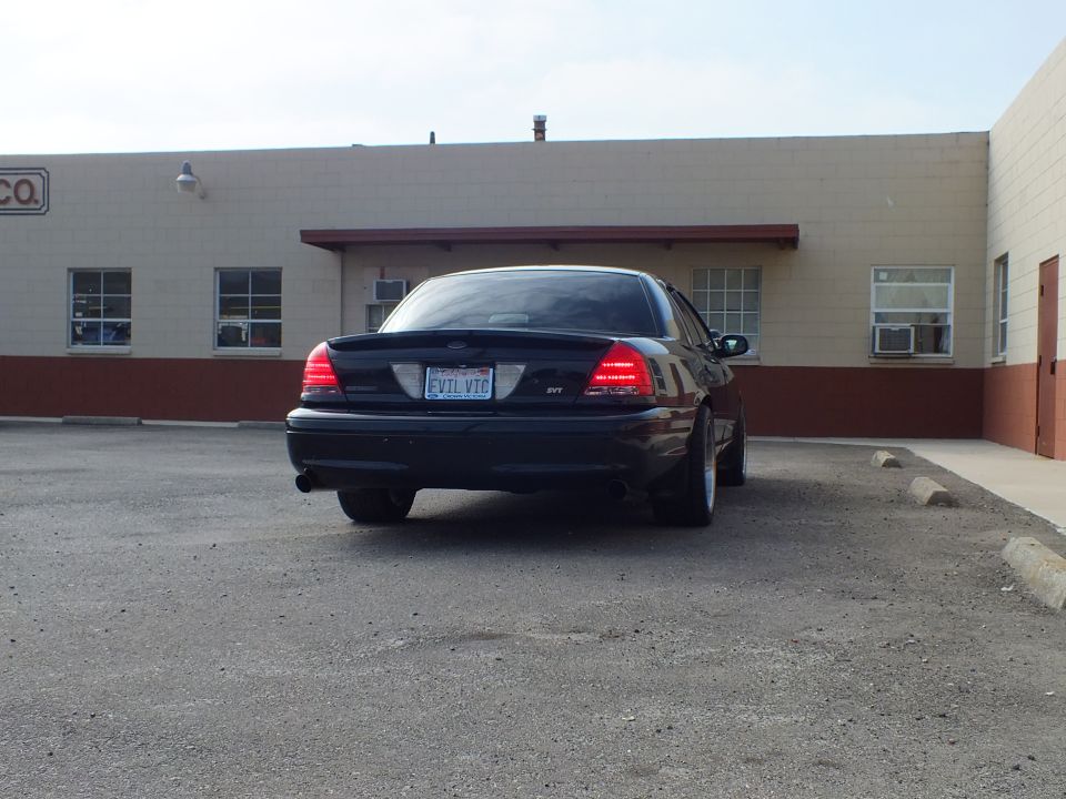Black Crown Victoria SVT rear three-quarter parked by tan building with awning