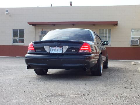 2003 Ford Crown Victoria - Rear three-quarter view of a black Crown Victoria on aftermarket wheels, EVIL VIC plate.