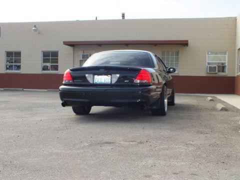 2003 Ford Crown Victoria - Rear three-quarter of a black Crown Victoria SVT parked in a lot before a tan masonry building.