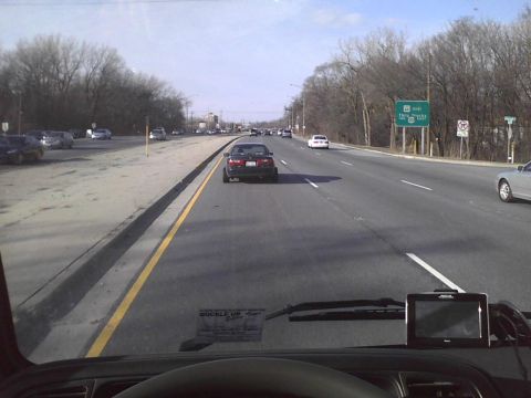 2003 Ford Crown Victoria - A dark sedan is seen from the perspective of another vehicle on a highway with trees lining the sides.