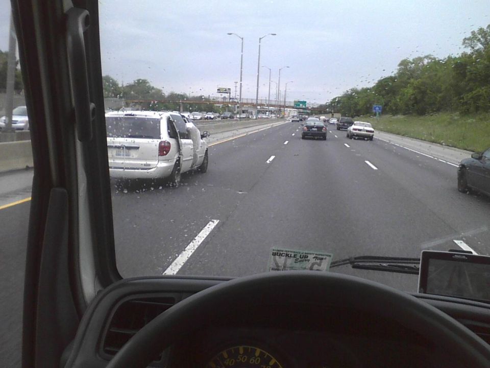 White minivan with open doors on a wet highway, viewed from inside a vehicle