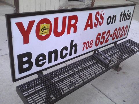 2003 Ford Crown Victoria - A bench sits outside with a sign advertising a phone number for a service.