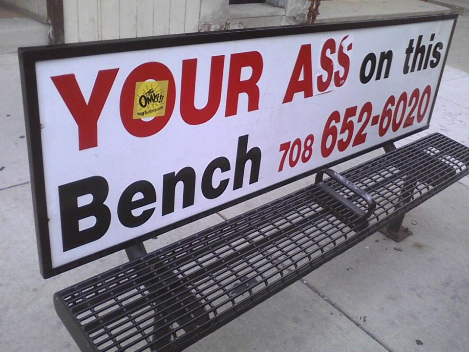Bench with sign that says 'YOUR ASS on this Bench' and a phone number
