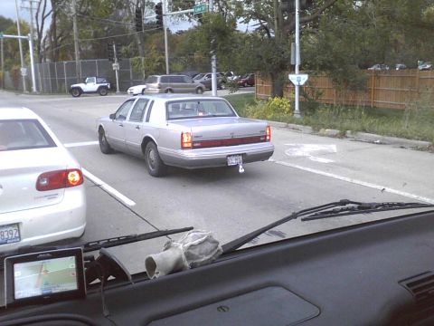 2003 Ford Crown Victoria - A silver Lincoln Town Car is seen from another vehicle's perspective on a city street.