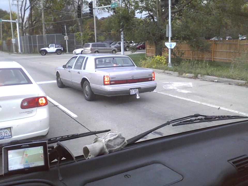 Silver Lincoln Town Car with a trailer hitch driving on a street, seen from another car