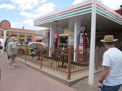 1991 Ford LTD Crown Victoria - A yellow car is parked at a vintage gas station with red gas pumps and a striped awning.