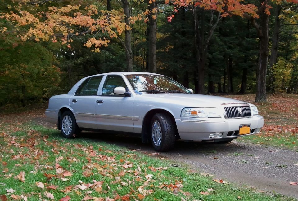 Silver 2008 Mercury Grand Marquis sedan parked on a gravel road with autumn foliage