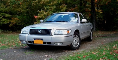 2008 Mercury Grand Marquis - A silver 2008 Mercury Grand Marquis is parked outdoors on a gravel path surrounded by trees.