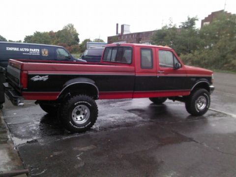 1993 Ford F-150 - A two-tone red and black pickup truck is parked on a wet asphalt surface, showing its side profile.
