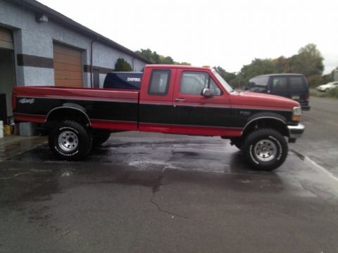 1993 Ford F-150 - This red and black Ford F-150 pickup truck is shown from the side, parked in front of a garage.