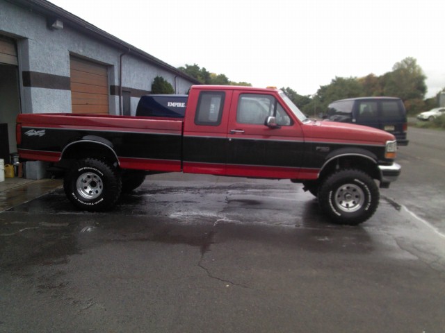 Red and black Ford F-150 pickup truck, side view, lifted suspension, off-road tires