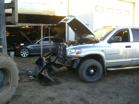 2005 Dodge 3500 - A silver Dodge pickup truck is undergoing repairs with its front bumper removed and hood open, while another vehicle sits in the background.
