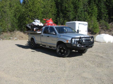 2005 Dodge 3500 - Silver 2005 Dodge 3500 pickup truck carrying two snowmobiles on its flatbed, parked outdoors.