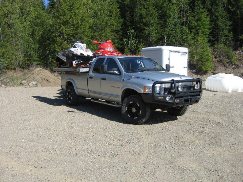 2005 Dodge 3500 pickup truck with two snowmobiles loaded on a flatbed in a gravel lot