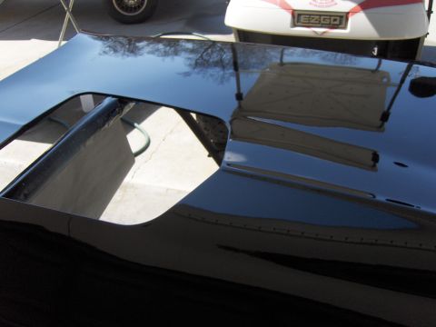 1973 Chevrolet Camaro - A black car hood with a prominent scoop is shown, reflecting the surrounding environment.