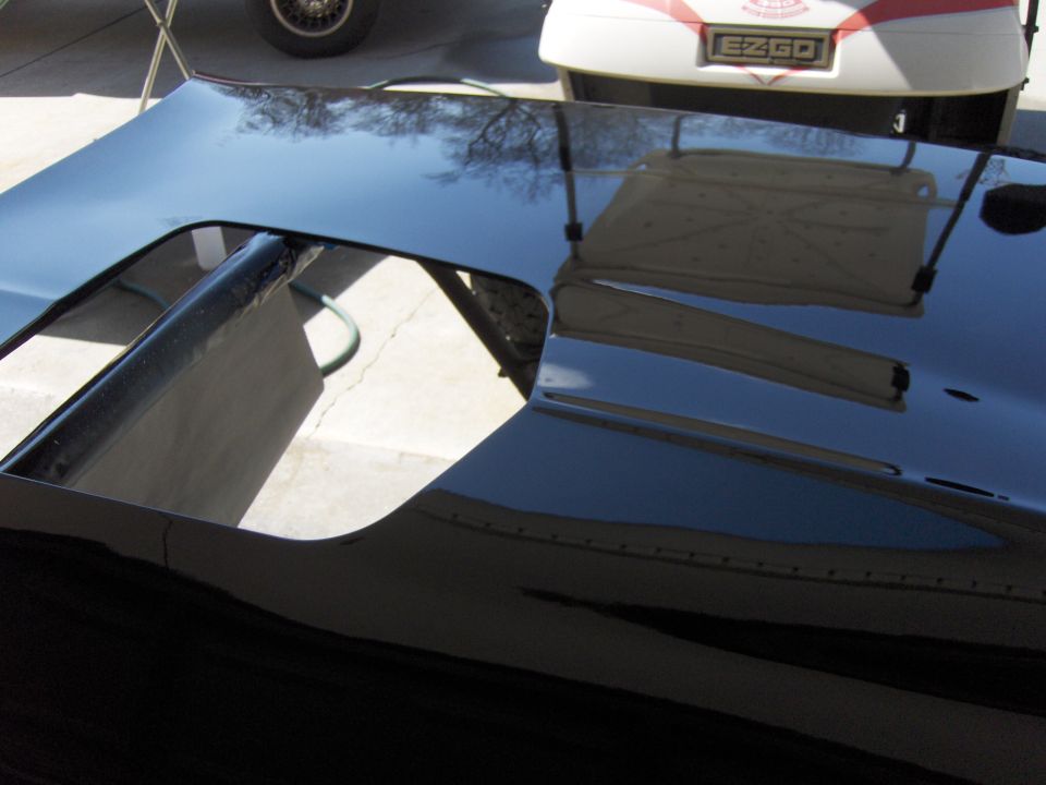 Black car hood with a large scoop opening, reflecting trees and a golf cart