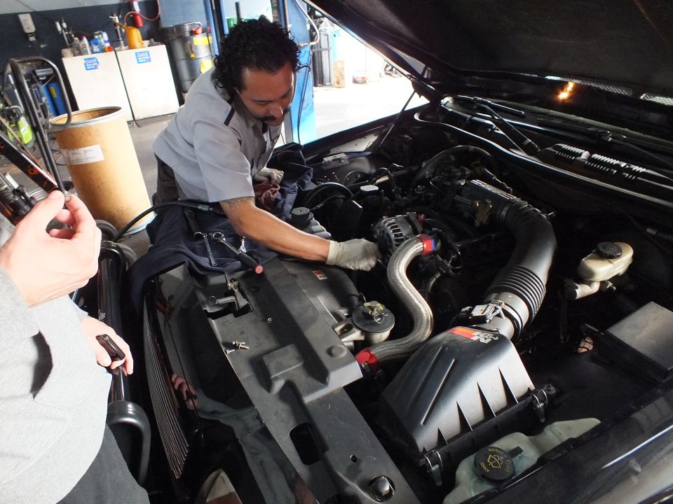 Mechanic in gray uniform working on engine bay with cold air intake under raised hood in repair shop