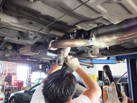 2003 Ford Crown Victoria - Worker reaches up to a driveshaft and exhaust line beneath a lifted car; ladder and vehicles fill the bay behind.