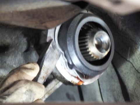 2003 Ford Crown Victoria - Detail of a splined slip yoke and retaining nut on a driveshaft, with a gloved hand bracing a tool below.