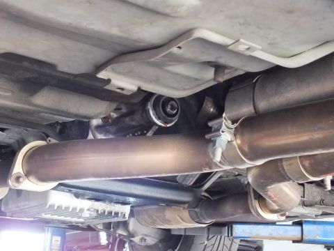 2003 Ford Crown Victoria - driveshaft passes between twin exhaust pipes and muffler canisters beneath a raised vehicle on a lift.