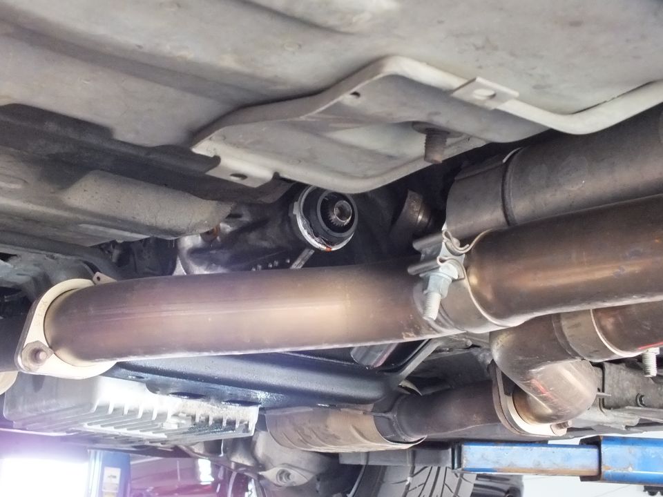 Underbody view of driveshaft running between dual exhaust pipes and mufflers on lifted vehicle