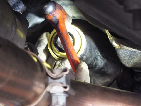 2003 Ford Crown Victoria - orange pry bar works against a seal at the transmission output while a gloved hand steadies it from below.